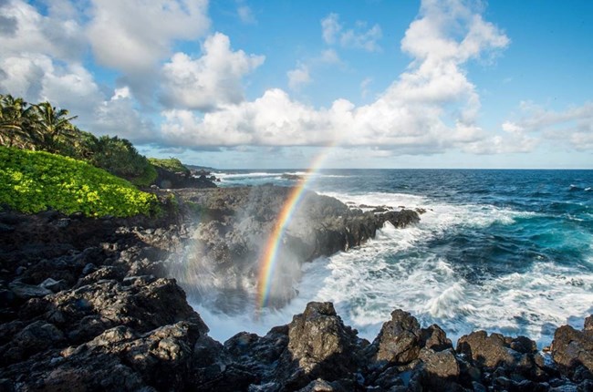 A rainbow forms in the mist of the ocean crashing on a rocky shore A rainbow forms in the mist of the ocean crashing on a rocky shore