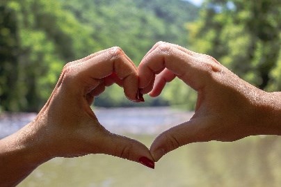 Two people put their hands together in the shape of a single heart with the Bluestone Wild and Scenic river in the background. NPS photo. Photo Credit: NPS
