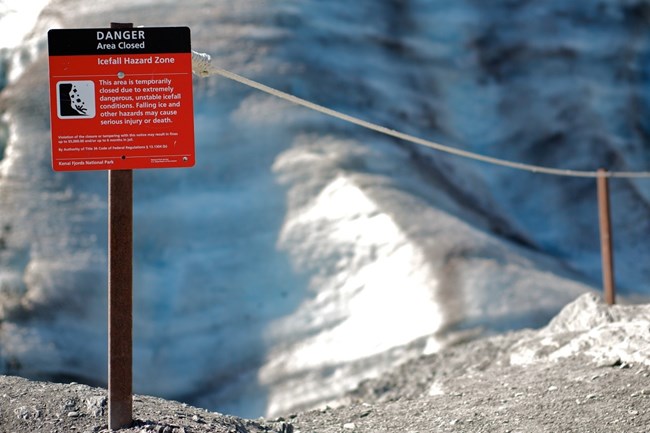 Hazard warning sign A red warning sign next to a roped area, in front of ice from a glacier.