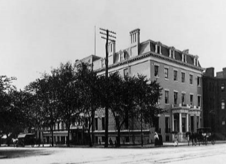 Historic Black and White photograph of James Wormley's five-story hotel. The hotel is surrounded by tall trees.