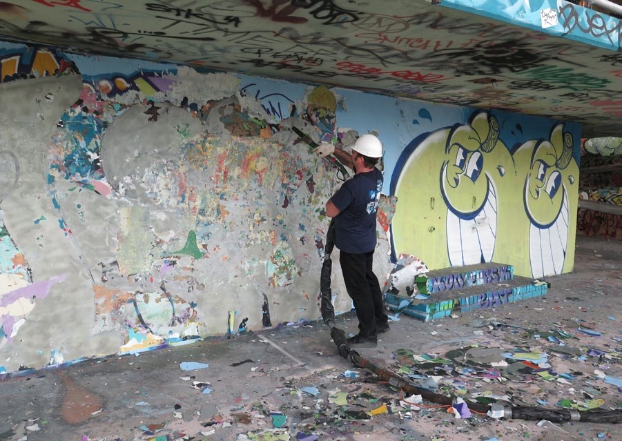 Preservationist holding a spray wand and removing paint from a concrete stadium