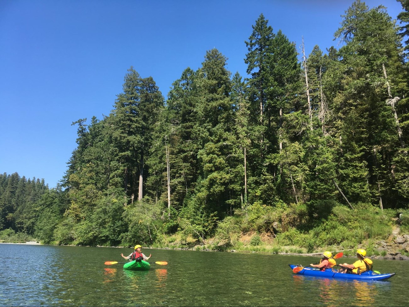 Kayaking on Smith Wild and Scenic River 3 boats spread out on the river wearing yellow safety gear.