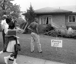a black man standing outside a house near a sign reading "danger keep out"