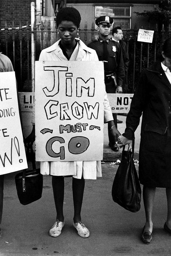 Black and white image of young woman holding a sign that say Jim Crow Must Go