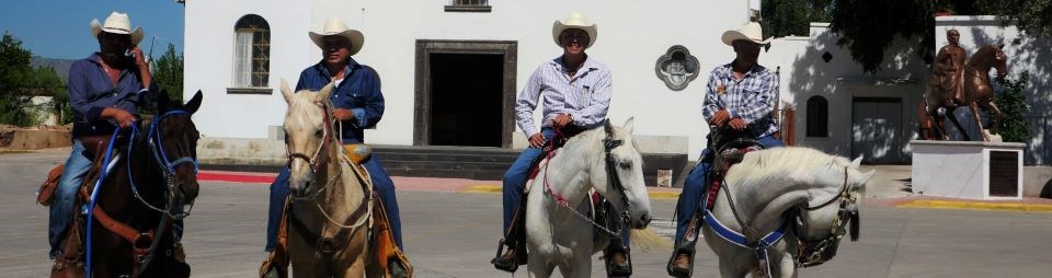 Four riders on horseback in front of a white church