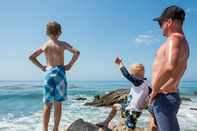 kids look out at waves in the ocean with excitement, while dad looks on.