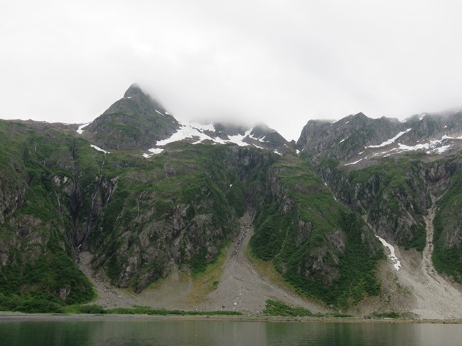 Loose rock forms multiple minor landslides from steep slopes into the water.