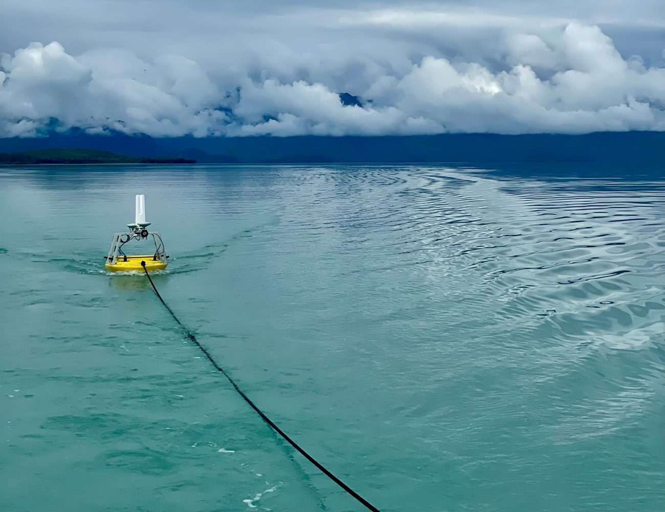 A small yellow boat is being pulled by a black rope through the water with clouds in the background.