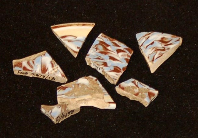 Photo of seven ceramic fragments with swirled design of yellow, brown, and blue.