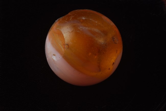 Glass marble, half amber-colored, half white.