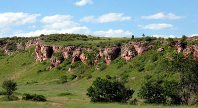 A cliff at Wind Cave National Park covered in green grass atop, red-brown jagged rocks