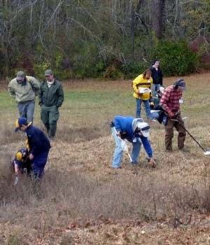 Men, women and children surveying a field with metal detectors.