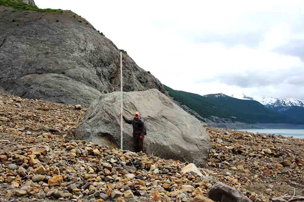 A large boulder with a man standing by it for scale.