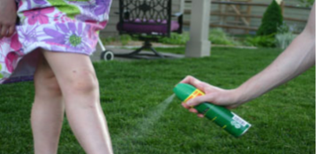 One person sprays bug spray on the legs of another person One person sprays bug spray on the legs of another person