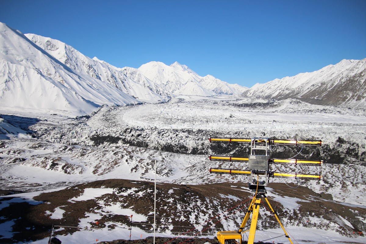 scientific equipment on a tripod overlooking a vast glacier and distant snowy mountains