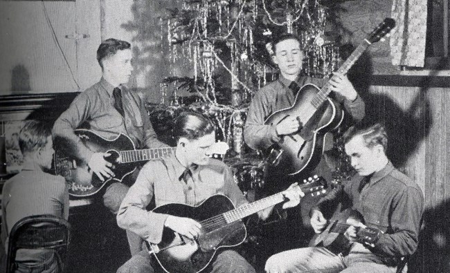 Black and white photo of four men playing guitars, wearing CCC uniforms.