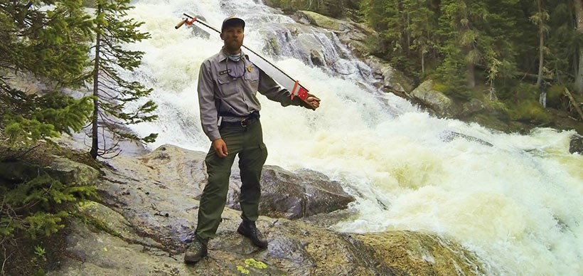 a ranger stands in front of a waterfall in a forest