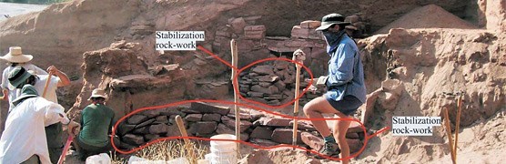 Stabilization rock work compared to the original rock work. The crew surrounds the fragile wall, holding shovels.