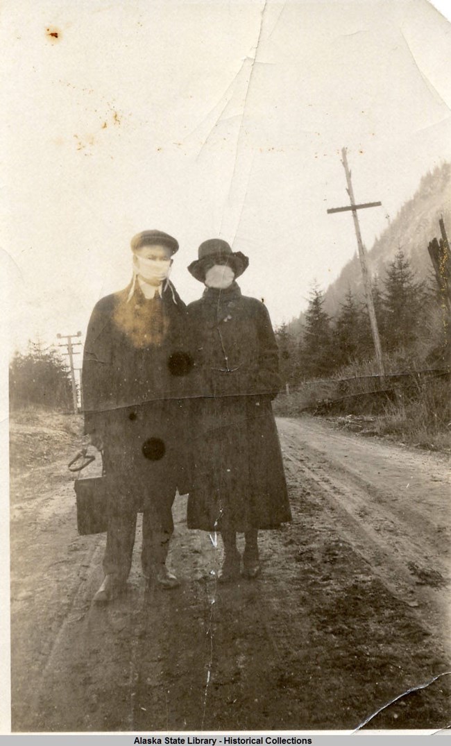 man and woman standing on a dirt road wearing white face-masks