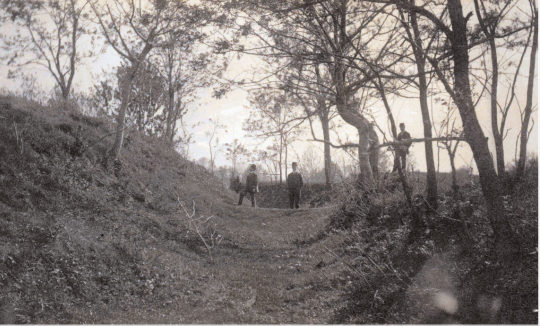 Photograph of three Soldiers at the Fort Stevens Parapet surrounded by trees. Two soldiers stand in the middle of two hills and one stands on the right hill.