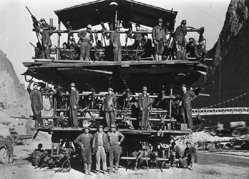 Workers lined up, standing on structure with drills in hand. (Bureau of Reclamation; Ben Glaha, photographer)