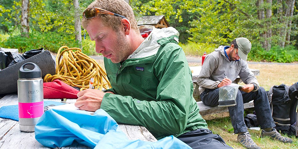 Two men sit with pads and pens writing