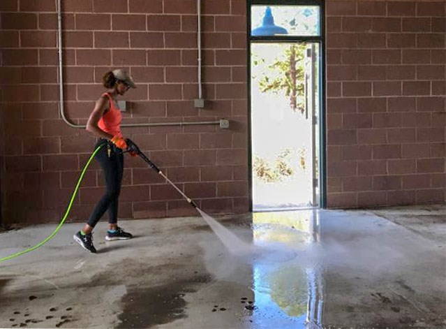 a woman is power washing a dirty garage floor