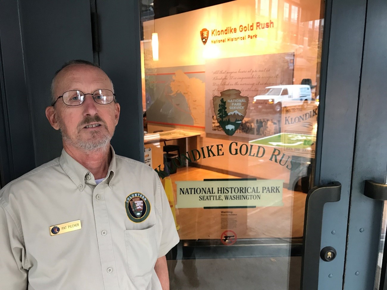 A man in a volunteer uniform poses in front of a door reading "Klondike Gold Rush"