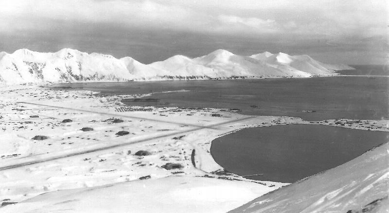 Black and white photo of snowy area and mountains along a bay