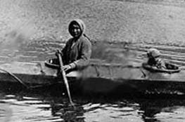 An Alutiiq adult and child travel in a kayak in this historic photo.