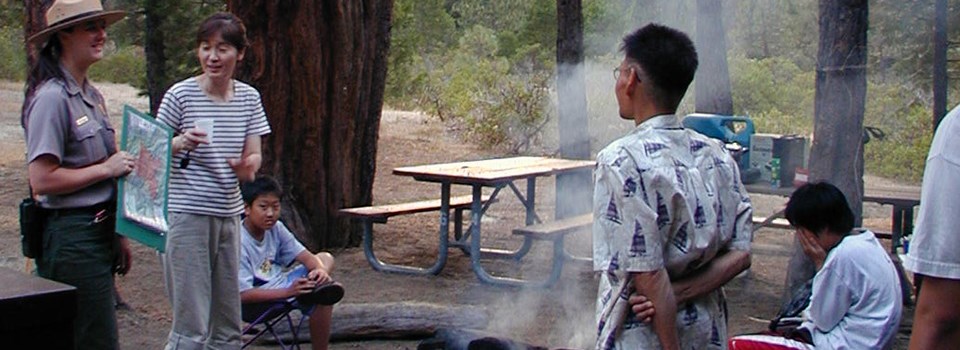 A ranger talks to campers around a campfire.