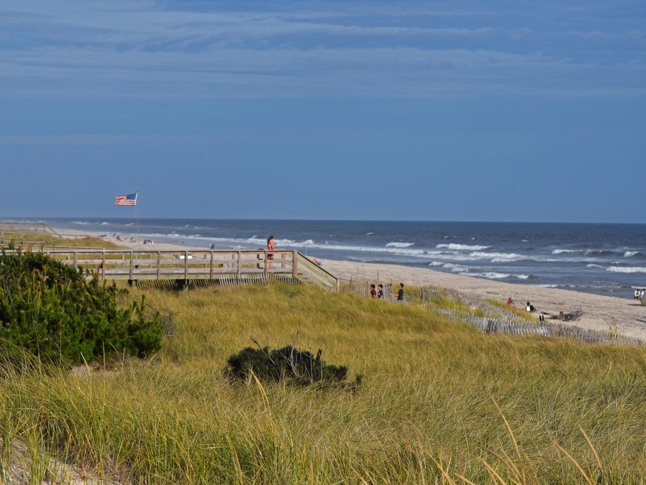 Girl stands on dune crossing overlooking beach and waves.