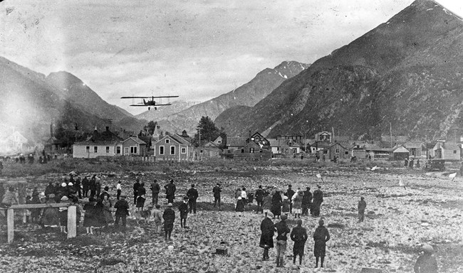 crowd of people watching plane fly low over houses