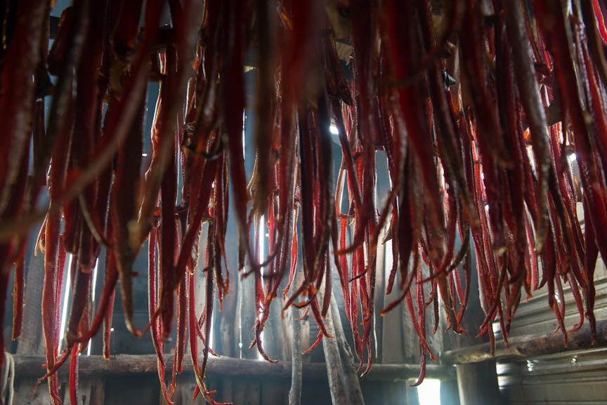 Long strips of drying salmon hang from the ceiling of a subsistence smokehouse.