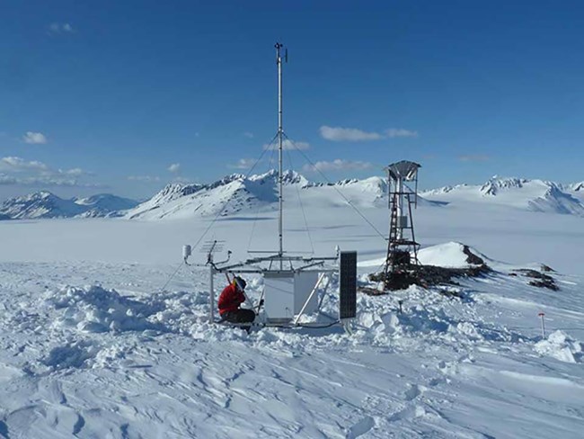 snowpack_CAKN_web A scientist works on weather station equipment high in the snow-covered mountains.