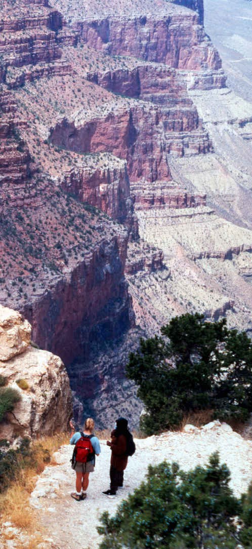 Hikers pause to take in the view on South Kaibab Trail. Hikers taking in the view on a steep Grand Canyon trail. In the distance a series of cliffs and ridgelines.