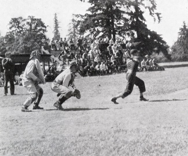 Black and white photo of baseball game with audience on bleachers in background.