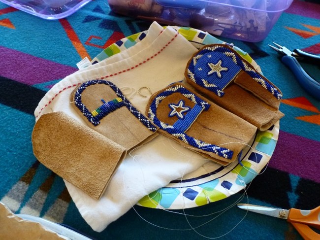 Moccasin making in progress Three child-size, unfinished leather moccasins sit on a colorful blanket