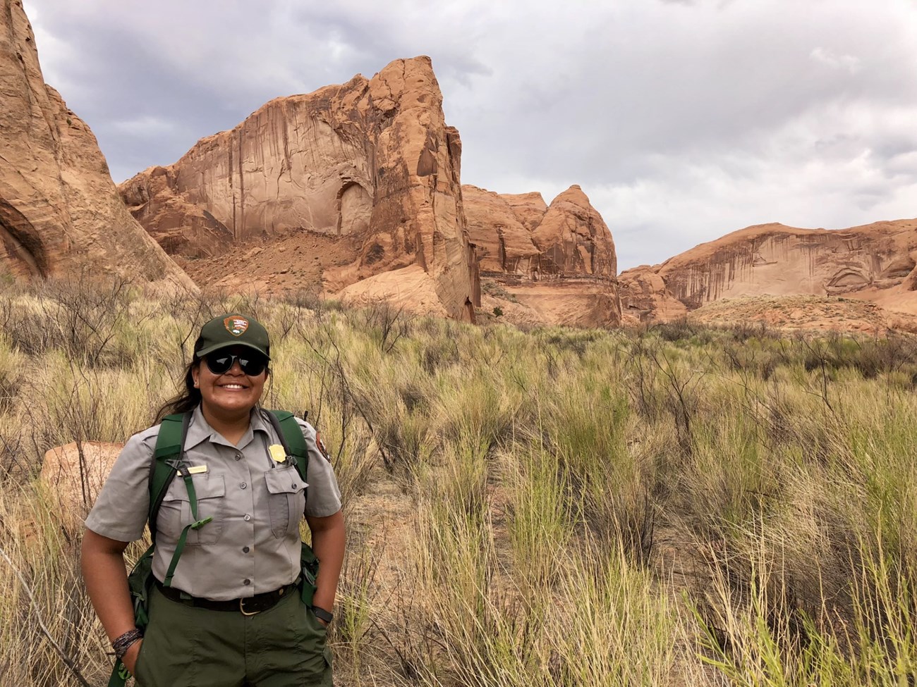 Diana Graymountain Park ranger wearing backpack stands at the bottom of a tall canyon