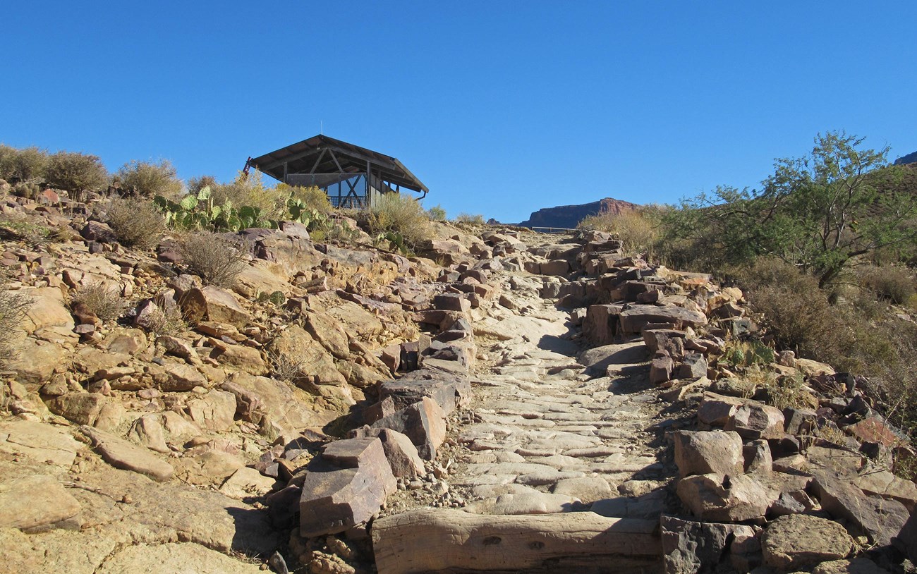 standing on a backcountry trail with rock liner sides. a small building is on the left, at the top of a hill