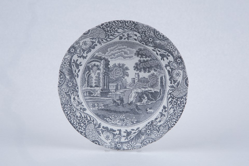 Small round plate with matte finish and the image of a rural scene in brown on it.