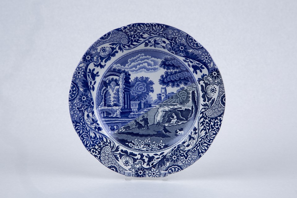 A small plate with a rural scene on it printed in blue. One half has been glazed and the colors are bright blues. The other half has not been glazed, and the colors are a duller blue.