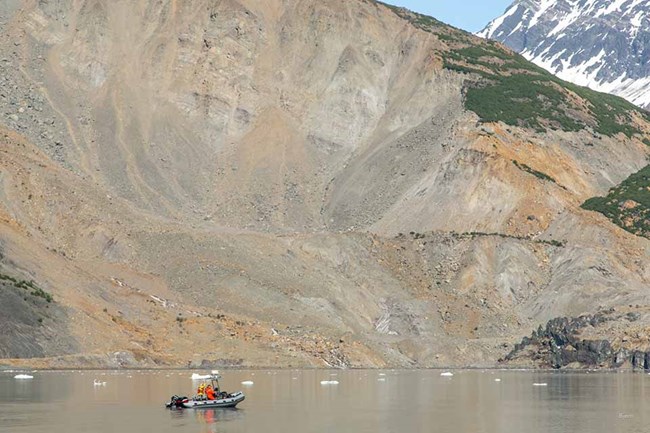 A boat of researchers is dwarfed by a massive coastal landslide.