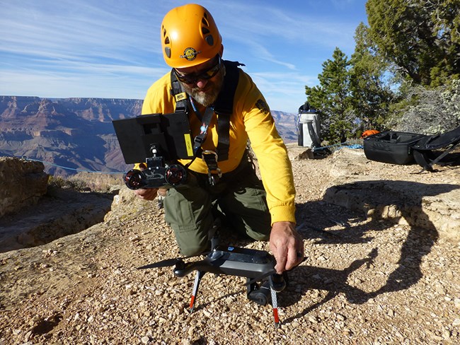 UAS Operator at Grand Canyon A man in Nomex and hardhat has a hand on quadcopter and controls.