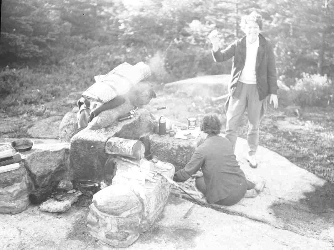 A 1950s Campfire in Acadia B&W photo of two individuals next to stone fire pit with smoke