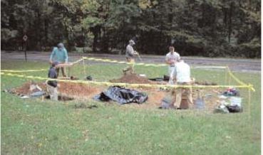 Yellow cautionary tape surrounds five archeologists excavating the Whitby Site.