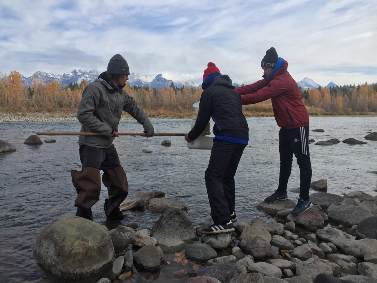 children use shovel and buckets to collect water samples along a roaring river.