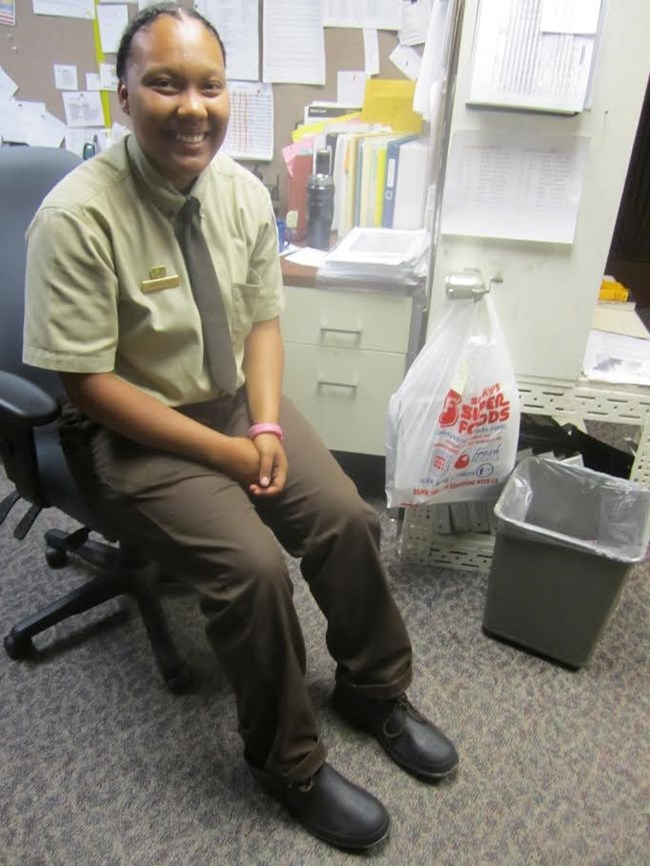 A ranger sits in a chair displaying rubber booties used in caves