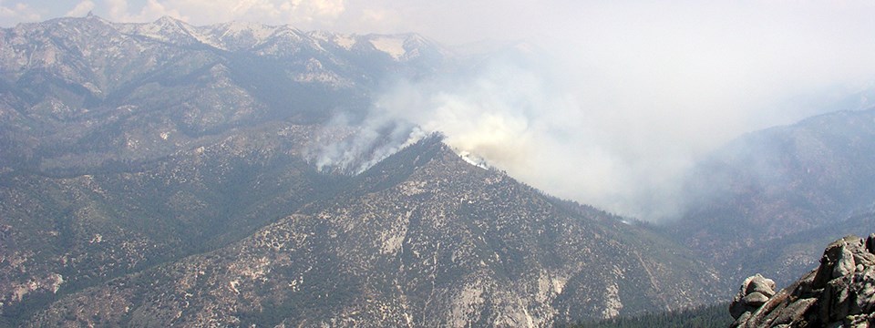 If a fire is located in a remote area and poses no threat to people or property, it may be monitored from the air. Smoke rises from rocky mountaintop.