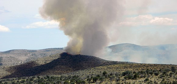 Smoke rises in a plume above a desert landscape.